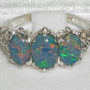 May include: A silver ring with three oval-shaped opals. The opals are a mix of blue, green, and red.