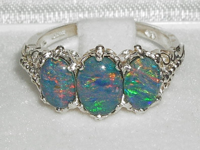 May include: A silver ring with three oval-shaped opals. The opals are a mix of blue, green, and red.