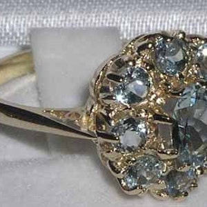 Pode incluir: Um anel de ouro com um grupo de pedras preciosas azuis claras engastadas em um design floral.