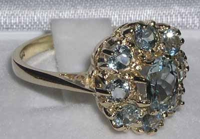 Pode incluir: Um anel de ouro com um grupo de pedras preciosas azuis claras engastadas em um design floral.