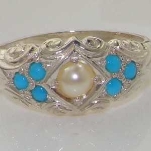 May include: A silver ring with a white pearl in the center and turquoise stones surrounding it. The ring has a detailed, ornate design.