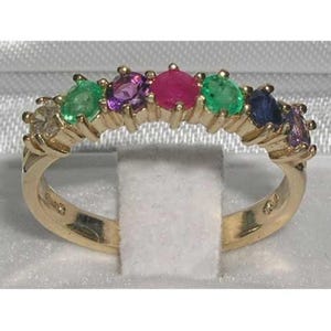 Puede incluir: Un anillo de oro con una fila de piedras preciosas de colores. Las piedras preciosas incluyen verde esmeralda, púrpura amatista, rojo rubí y azul zafiro. El anillo está engastado en una banda de oro.