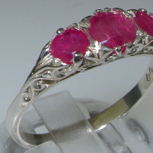 May include: A silver ring with three red ruby stones set in a delicate filigree design.