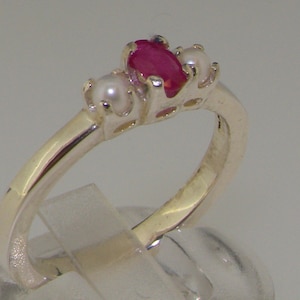 May include: A silver ring with a red ruby and two white pearls. The ring is set in a simple band.