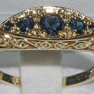 May include: A gold ring with a decorative design and three blue sapphires.