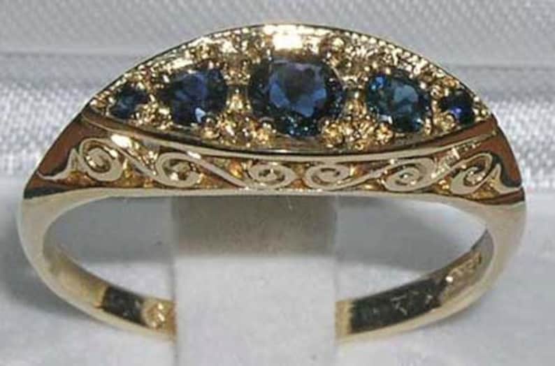 May include: A gold ring with a decorative design and three blue sapphires.