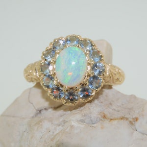 May include: A gold ring with a large oval opal gemstone surrounded by a halo of smaller blue gemstones.