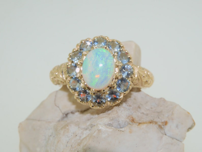 May include: A gold ring with a large oval opal gemstone surrounded by a halo of smaller blue gemstones.