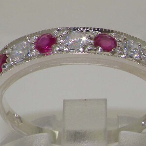 May include: A silver band ring with a row of alternating red ruby and clear round stones.