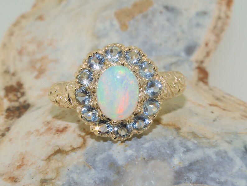 May include: A gold ring with a white opal gemstone surrounded by a halo of blue topaz stones.
