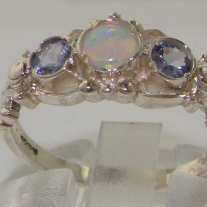 May include: A silver ring with an opal and two blue gemstones. The ring has a detailed design with intricate carvings.