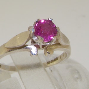 以下が含まれることがあります： 繊細な花柄のデザインにピンクの宝石がセットされたシルバーリング。リングの内側に「925」の刻印があります。