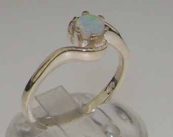 Puede incluir: Un anillo de plata con una piedra de ópalo blanco. El anillo tiene una banda curva y un diseño simple.