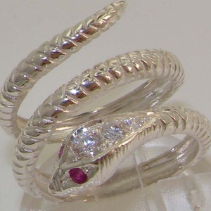 Op de afbeelding: Een zilveren slangenring met een robijnoog en heldere zirkonia-stenen. De slang is om de ringband gewikkeld.