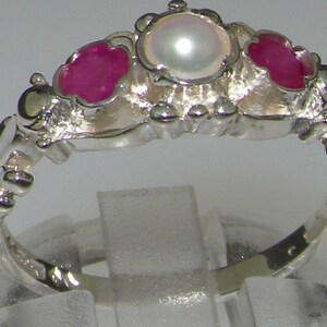 May include: A silver ring with a pearl and two ruby stones. The ring has a delicate, ornate design.