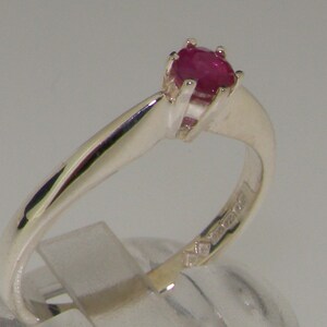 May include: A silver ring with a red ruby gemstone set in a prong setting. The ring is simple and elegant.
