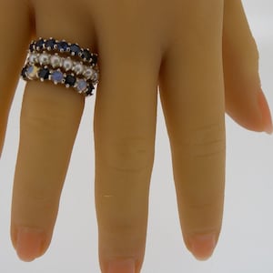 以下が含まれることがあります： 宝石がついた金の指輪が3つ。一番上の指輪は青い宝石、真ん中の指輪は白い真珠、一番下の指輪は薄い青色の宝石がついています。