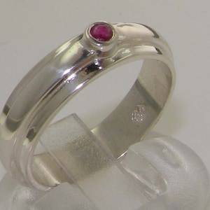 May include: A silver band ring with a single red gemstone set in the center.