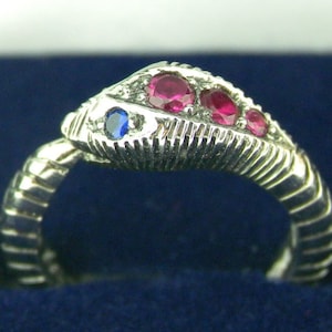 May include: Silver ring with a snake design. The snake is adorned with red and blue gemstones.