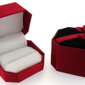 May include: Two red velvet ring boxes. One box is open and has a white velvet interior. The other box is closed and has a red ribbon and bow.