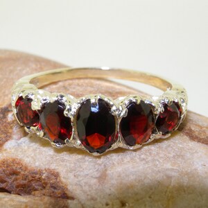 May include: A gold band ring with five oval-shaped red gemstones set in a decorative design.