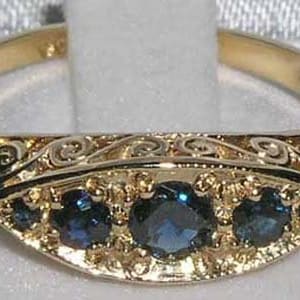 May include: A gold ring with a black enamel band and five blue sapphires. The band is decorated with an intricate scroll design.