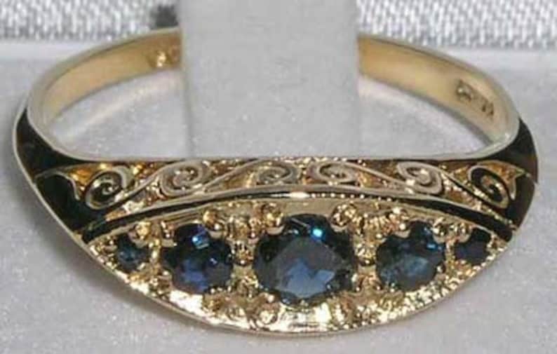 May include: A gold ring with a black enamel band and five blue sapphires. The band is decorated with an intricate scroll design.
