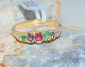 May include: A gold band ring with five gemstones. The gemstones are a ruby, two emeralds, a sapphire, and a diamond.