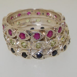 May include: Three silver rings with a stackable design. The top ring features pink gemstones, the middle ring features green gemstones, and the bottom ring features blue gemstones.