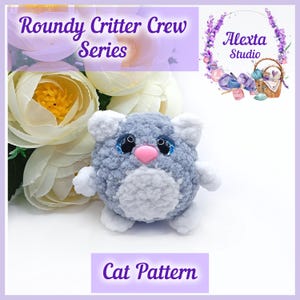 Op de afbeelding: Een gehaakte grijze kattenknuffel met witte accenten, een roze neus en blauwe ogen. De afbeelding bevat de tekst "Roundy Critter Crew Series" en "Cat Pattern". Het logo "Alexta Studio" is ook zichtbaar.