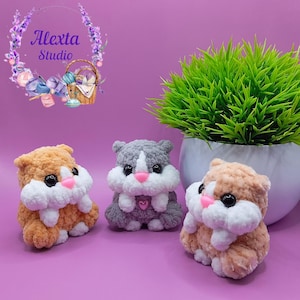 May include: Three handmade crochet hamster toys in shades of orange, gray, and tan. Each plush hamster has black eyes, a pink nose, and white fluffy accents. The background is a solid purple with a green plant in a white pot.