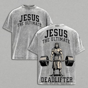 May include: Two light gray t-shirts. The front shirt has the text "JESUS THE ULTIMATE" in black. The back of the second shirt features an illustration of Jesus as a deadlifter, with the text "JESUS THE ULTIMATE" above and "DEADLIFTER" below.