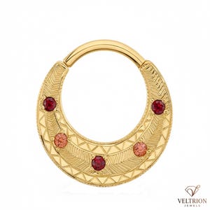 May include: A gold hoop ring featuring a textured surface with engraved chevron and triangular patterns. The ring is set with five round gemstones in alternating shades of deep red and lighter pink, arranged along the lower curved section.