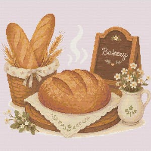 Op de afbeelding: Een kruissteekpatroon met een rond brood op een doek, een mand gevuld met stokbroden en tarwestengels, een kleine kan met witte bloemen en een houten bord met het woord Bakery in wit cursief schrift.