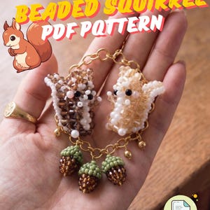 Op de afbeelding: Een PDF-patroon van een kralen eekhoorn wordt getoond. Twee kralen eekhoorn bedels zijn verbonden door een gouden ketting, met drie kralen eikel bedels die eronder hangen. De eekhoorns zijn bruin en wit, met zwarte kraalogen. De tekst "Beaded Squirrel PDF Pattern" staat in de afbeelding.