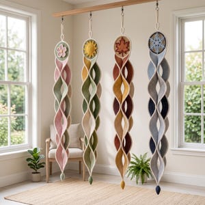 May include: Four vertical hanging spiral decorations made of crocheted fabric, each featuring a circular top with a seasonal icon: a pink flower, a yellow sun, an orange maple leaf, and a blue snowflake, with color-coordinated twisted fabric tails.
