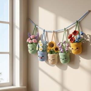 May include: Six crocheted hanging flower pots, each with a smiling face and filled with colourful yarn flowers. The pots are suspended from a blue rope, creating a cheerful, handmade decorative display.