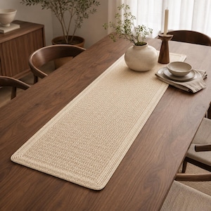 May include: A rectangular beige table runner featuring a woven, textured surface with a thick, braided border. The runner is centered on a dark brown wooden dining table, providing a neutral foundation for the decorative items placed upon it.