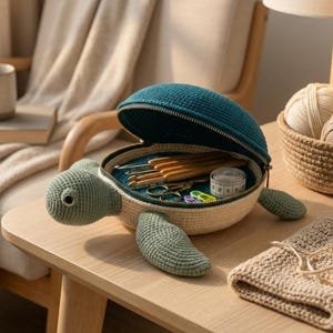 May include: A turtle-shaped crochet storage case with a dark teal shell that opens with a zipper. The body is light beige with sage green head and flippers. Inside, the case holds wooden crochet hooks, metal scissors, and a measuring tape.