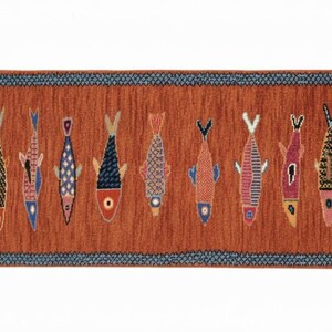 May include: A rectangular runner rug with a burnt orange background featuring a row of twelve stylized fish in various colors and patterns. The rug is framed by a dark blue border with a repeating geometric design and has short white fringe at both ends.