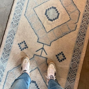 May include: A rectangular area rug featuring a cream-colored base with a repeating geometric pattern in shades of blue. The design includes central diamond shapes, smaller square motifs, and a border composed of repeating arrow-like symbols.