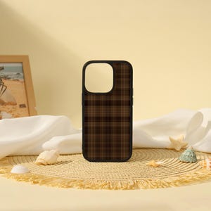 Peut inclure: Une coque de smartphone rectangulaire arborant un motif à carreaux marron foncé et noir. La coque présente un contour noir et une grande découpe carrée dans le coin supérieur gauche pour l'objectif de l'appareil photo, avec des lignes croisées.