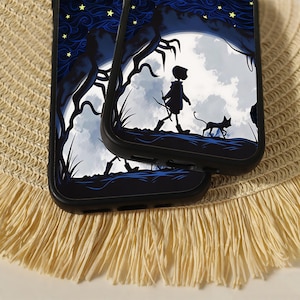 May include: Two black smartphone cases featuring a graphic illustration of a silhouette of a person walking with a cat under a large white moon, surrounded by dark blue swirling clouds and yellow stars against a dark blue night sky background.