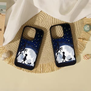 May include: Two black smartphone cases featuring a graphic illustration of a silhouette of a person and a small cat walking under a large white moon against a dark blue starry sky with swirling patterns and dark tree branches on the sides.