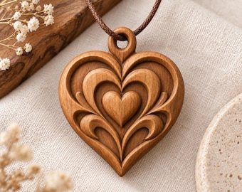 May include: A heart-shaped wooden pendant featuring intricate, layered carved details and a central raised heart motif. The pendant is suspended from a thin, dark brown cord, showcasing a smooth, polished finish with visible wood grain patterns.
