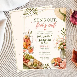 May include: A cream-colored party invitation card featuring a straw hat, string lights, a pitcher of sangria, a charcuterie board, and a vase of flowers. The text reads: SUN'S OUT, fun's out, JOIN THE ANDERSON'S FOR AN AFTERNOON OF sun, swim & sangria, JULY 12, 03:00 PM.
