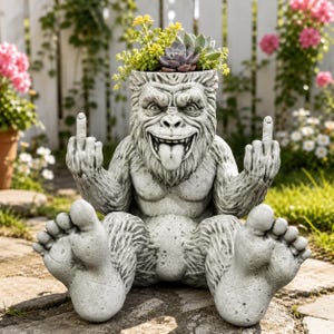 May include: A gray stone-effect planter shaped like a seated gorilla with a textured fur finish, a wide grin, and its tongue sticking out. The gorilla is holding both middle fingers up in a gesture, with a small succulent plant growing from its head.