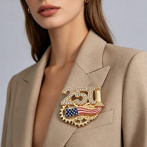 May include: A gold-toned brooch with the number "250" encrusted with rhinestones, an American flag, and a gear design. The brooch is pinned to a tan blazer.