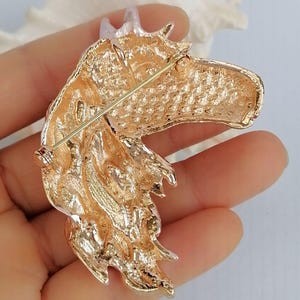 K&ouml;nnte beinhalten: Eine goldfarbene Pferdekopfbrosche. Die Brosche ist mit strukturierten Oberfl&auml;chen und einem Nadelverschluss auf der R&uuml;ckseite versehen. Der Pferdekopf hat eine M&auml;hne und ein detailliertes Gesicht. Die Brosche ist wahrscheinlich aus Metall.