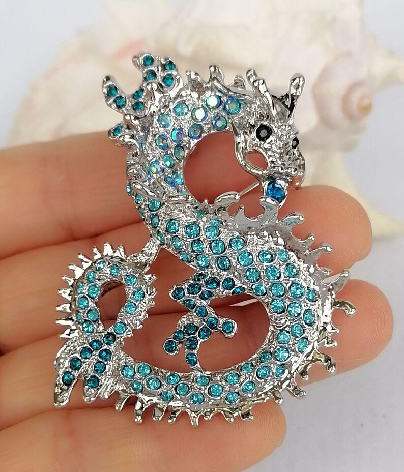 Puede incluir: Broche de drag&oacute;n plateado con pedrer&iacute;a turquesa. El drag&oacute;n presenta un cuerpo texturizado y un dise&ntilde;o intrincado. Un accesorio decorativo para ropa o bolsos.